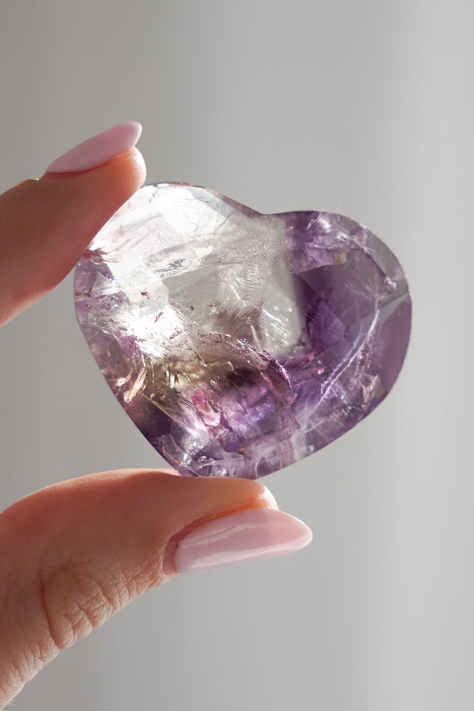 Hand holding a large amethyst crystal against a neutral background