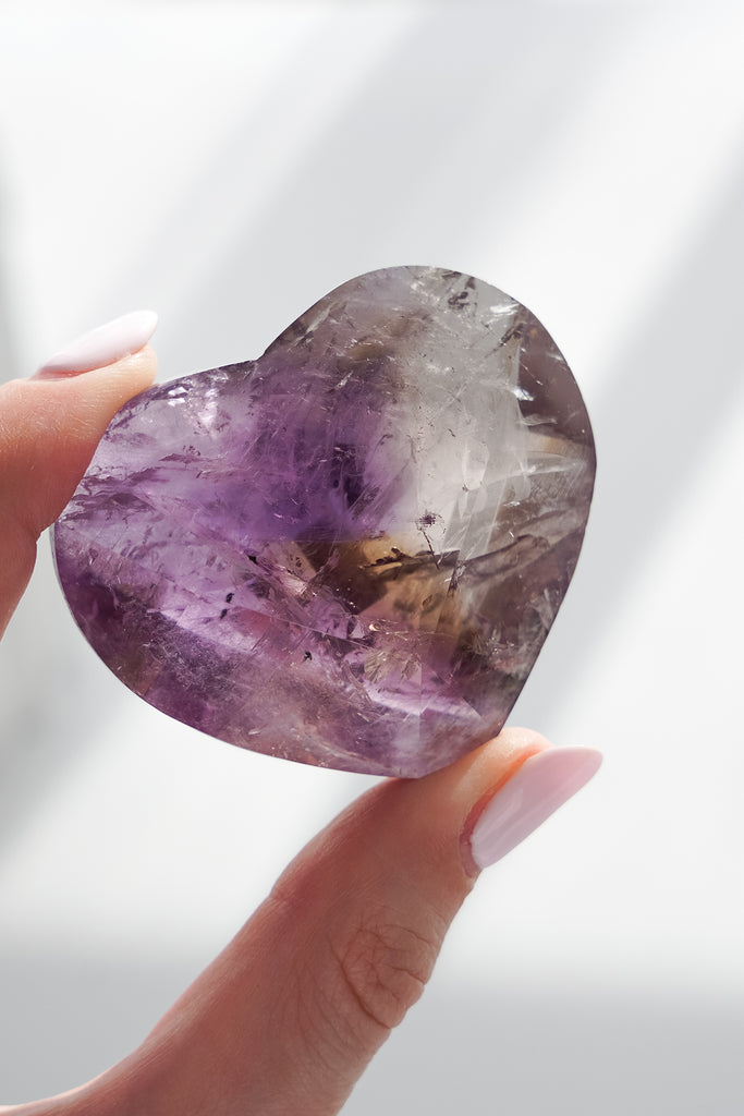 Heart-shaped amethyst crystal held by a hand against a light background