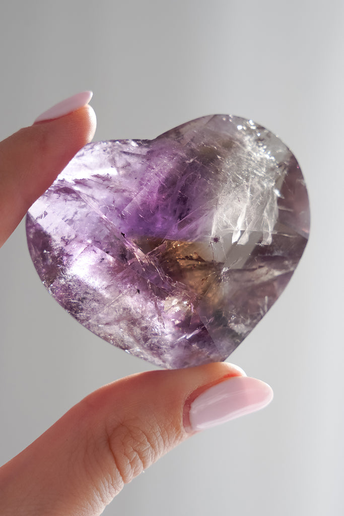 Heart-shaped purple crystal held by a hand against a light gray background