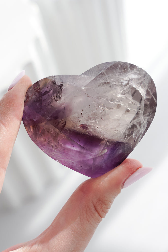 Heart-shaped amethyst crystal held by a hand against a white background