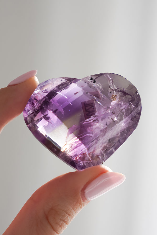 Heart-shaped purple crystal held by a hand against a light background