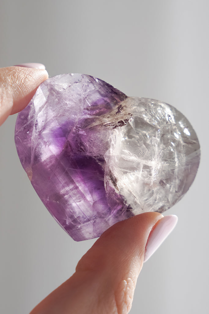 Hand holding a purple and clear crystal against a neutral background