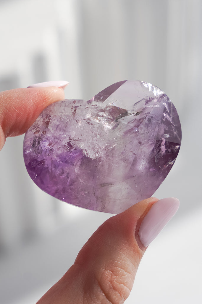 Hand holding a purple crystal against a blurred background
