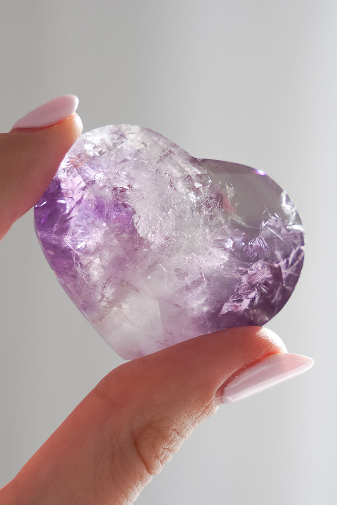 Person holding a large crystal with purple and white colors against a plain background