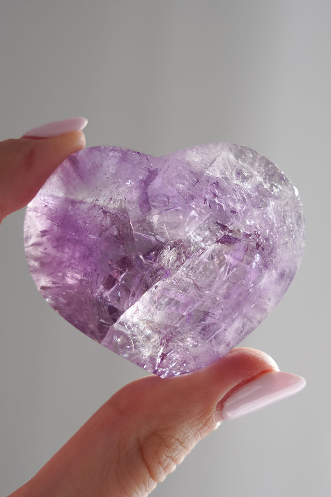 Heart-shaped purple crystal held by a hand against a gray background