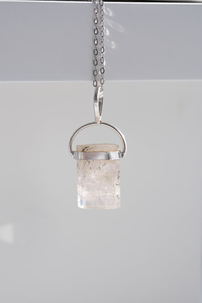 Small pendant with a cylindrical clear stone and silver chain on a light gray background