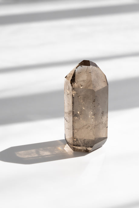 Smoky quartz crystal on a white surface with soft shadows