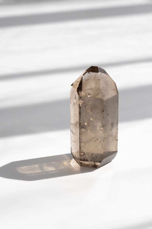 Smoky quartz crystal on a white surface with soft shadows
