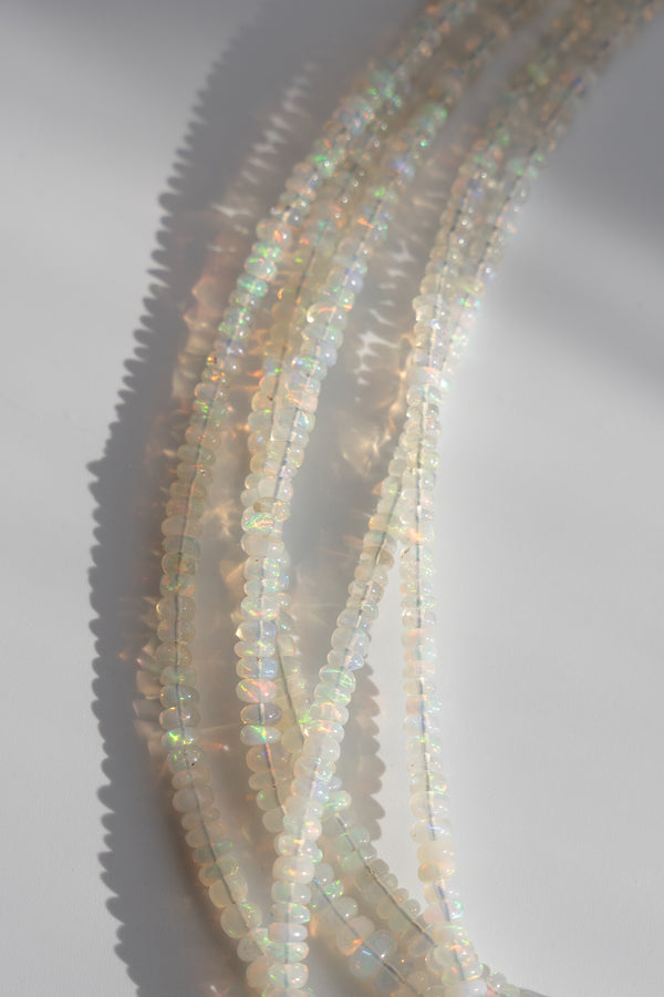 Multiple strands of small faceted beads with an iridescent opal-like finish, arranged on a light gray background with soft shadows.